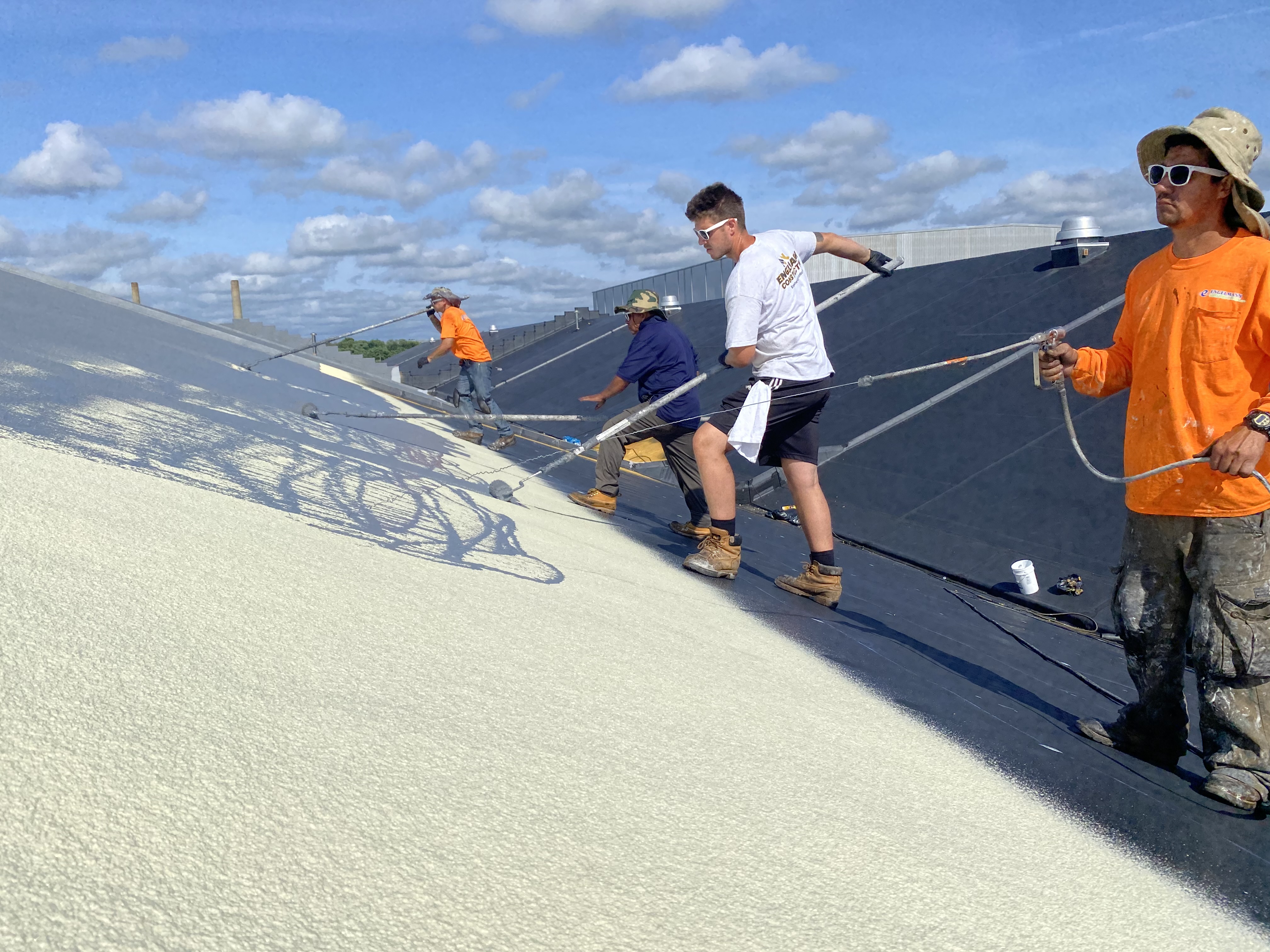Engelmann Construction workers applying a gray liquid coating on a commercial roof with rollers