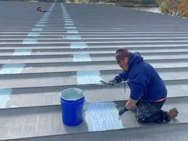 Worker applying a heavier roof coating on a commercial roof's main leak points